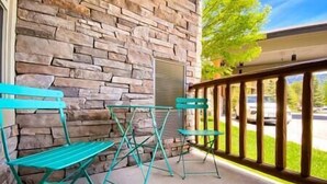Eine Terrasse mit Steinmauer, Metallgeländer und zwei grünen Klapptischen.