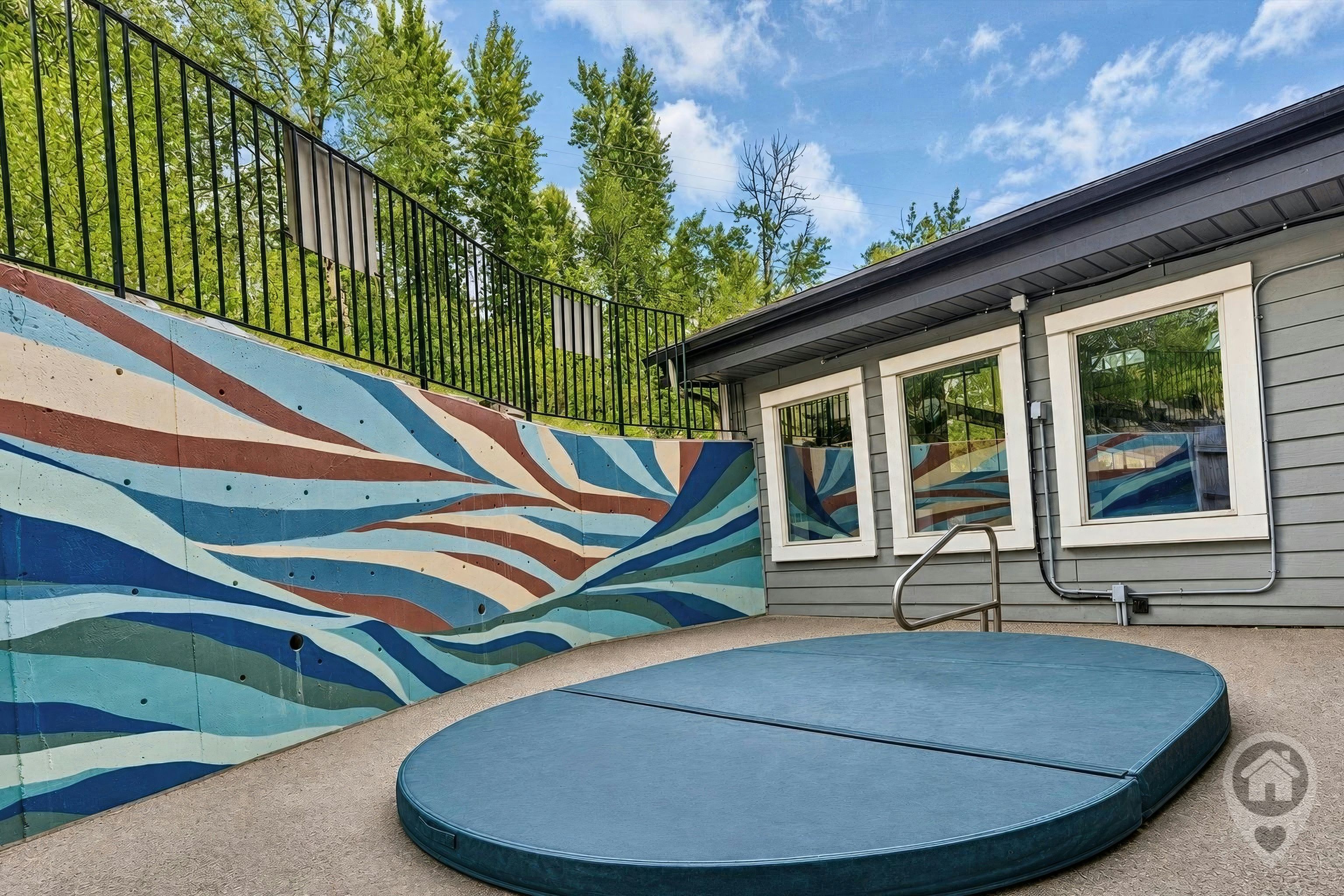 Une piscine agrémentée d’une fresque murale colorée, d’un plongeoir et d’une maison en arrière-plan.