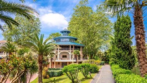 A traditional-style building with a blue roof, surrounded by lush greenery and palm trees.