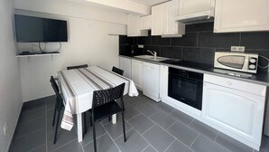 A compact kitchen with white cabinets, a black countertop, a microwave, and a dining area with a striped tablecloth.