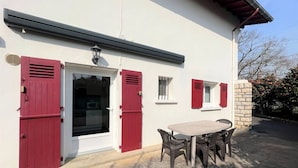 A building with a white exterior, red shutters, a door, and a table with chairs outside.