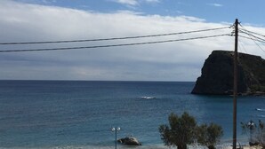 Vista costiera con scogliera rocciosa, mare blu cristallino e linee elettriche.