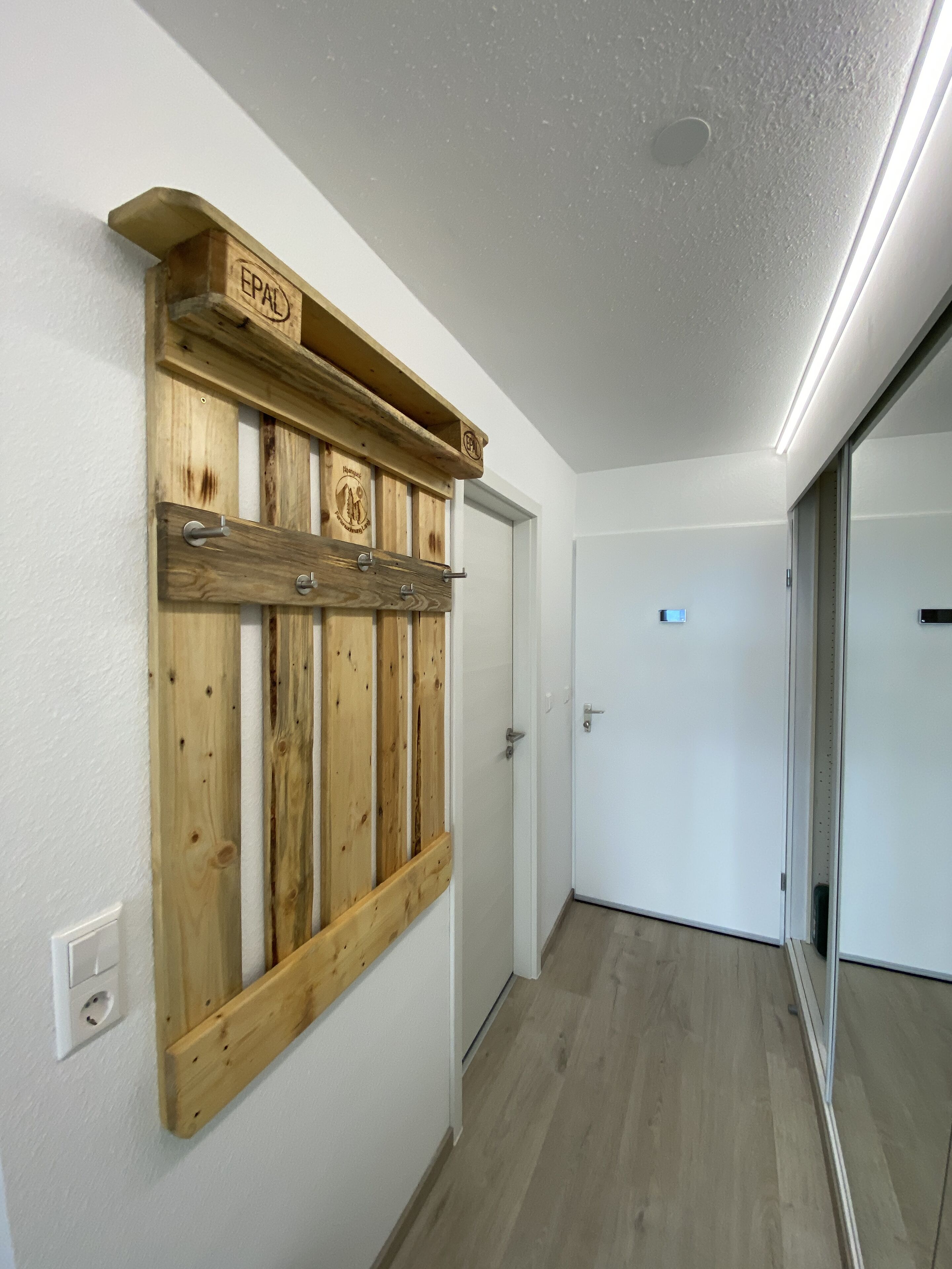 A hallway with a wooden wall-mounted rack labeled "EPAL" and a door with a small sign.
