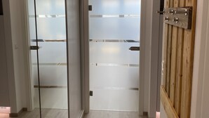 A modern hallway with a sliding glass door, a wooden shelf with hooks, and a frosted glass partition. - FeWo Längl - modern "Alpenguck" apartment with pool and sauna in the Allgäu (Scheidegg)