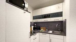 A compact kitchen with white cabinets, a black countertop, and a stainless steel sink. - FeWo Längl - modern "Alpenguck" apartment with pool and sauna in the Allgäu (Scheidegg)