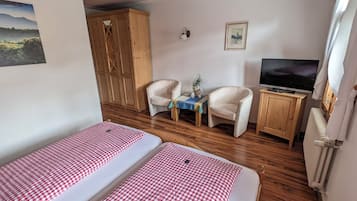 Una habitación con dos camas, televisión, una mesita con una planta y un armario de madera.