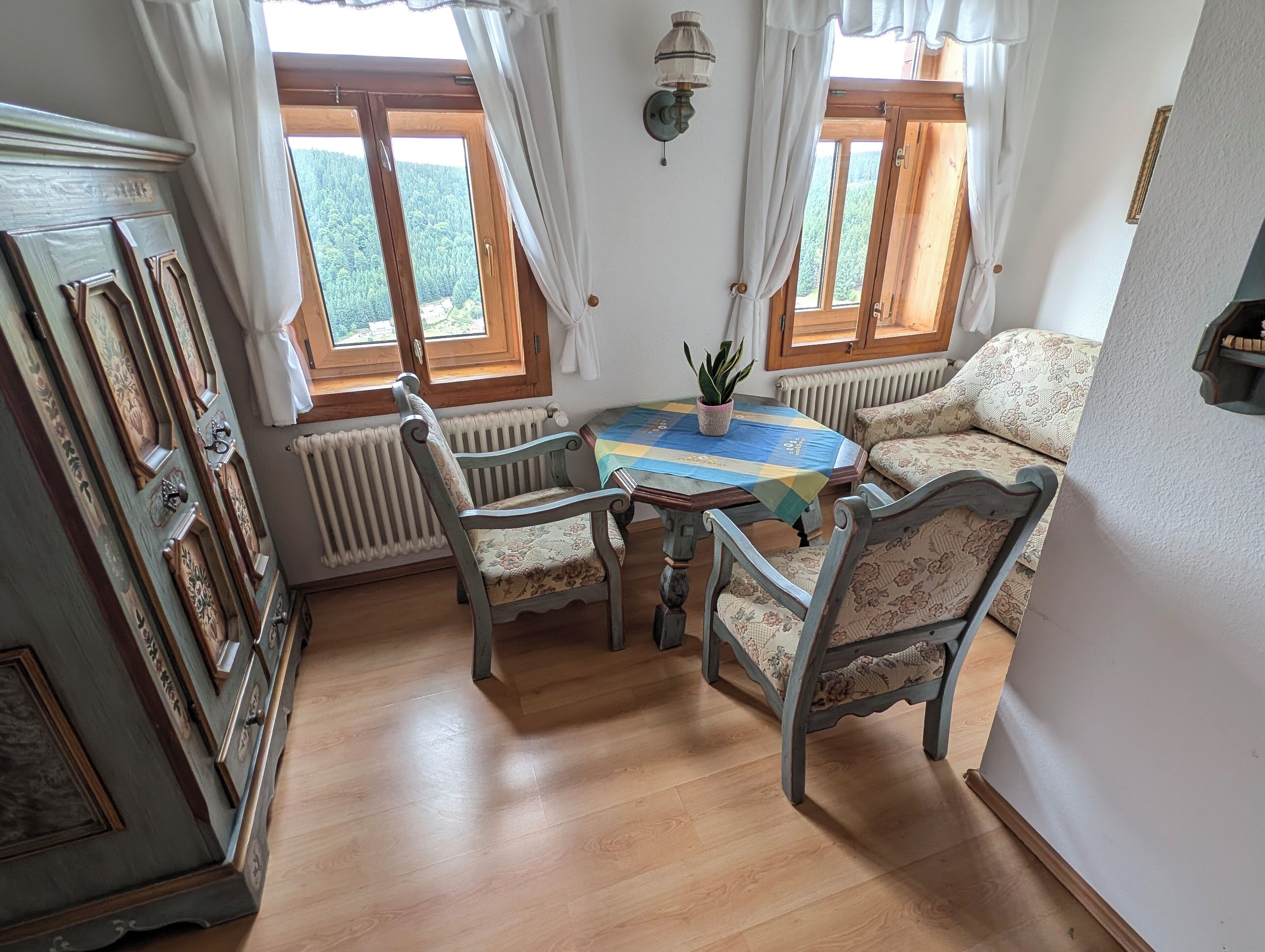 Una habitación acogedora con suelo de madera, una mesa redonda con sillas, un sofá y un radiador.