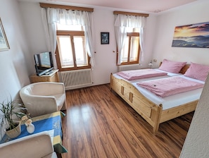 Ein Zimmer mit zwei Holzbetten, einem Schreibtisch mit Computer, einem Stuhl, einem Heizkörper und einem Fenster mit Vorhängen.