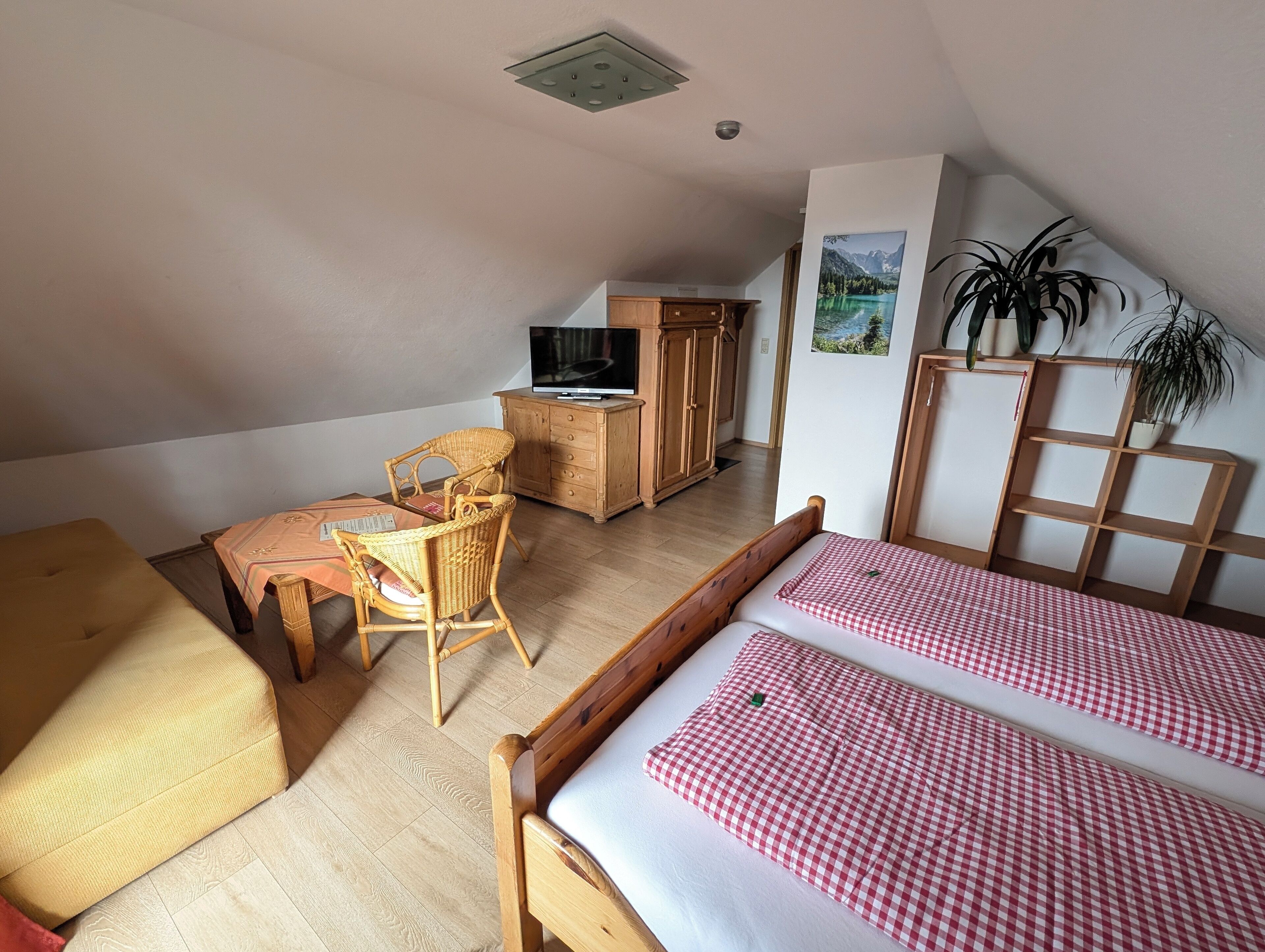 Una habitación cálida en el ático con una cama de madera, una silla de mimbre, una mesita y un televisor sobre un mueble de madera.