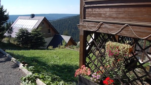 A wooden cabin with a sloped roof, a wooden deck, and a garden with flowers.