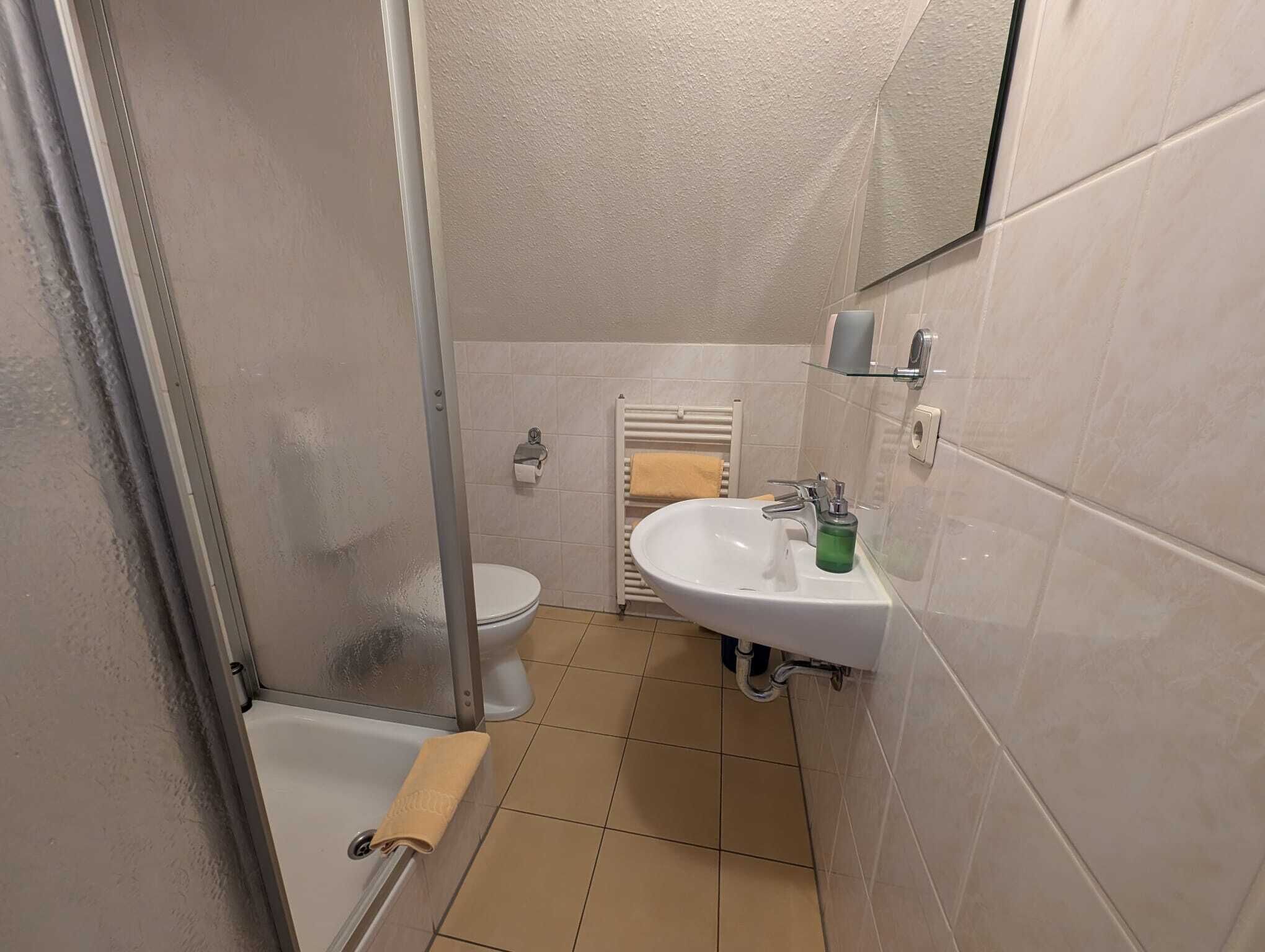 A bathroom with a shower, toilet, sink, and a towel rack.