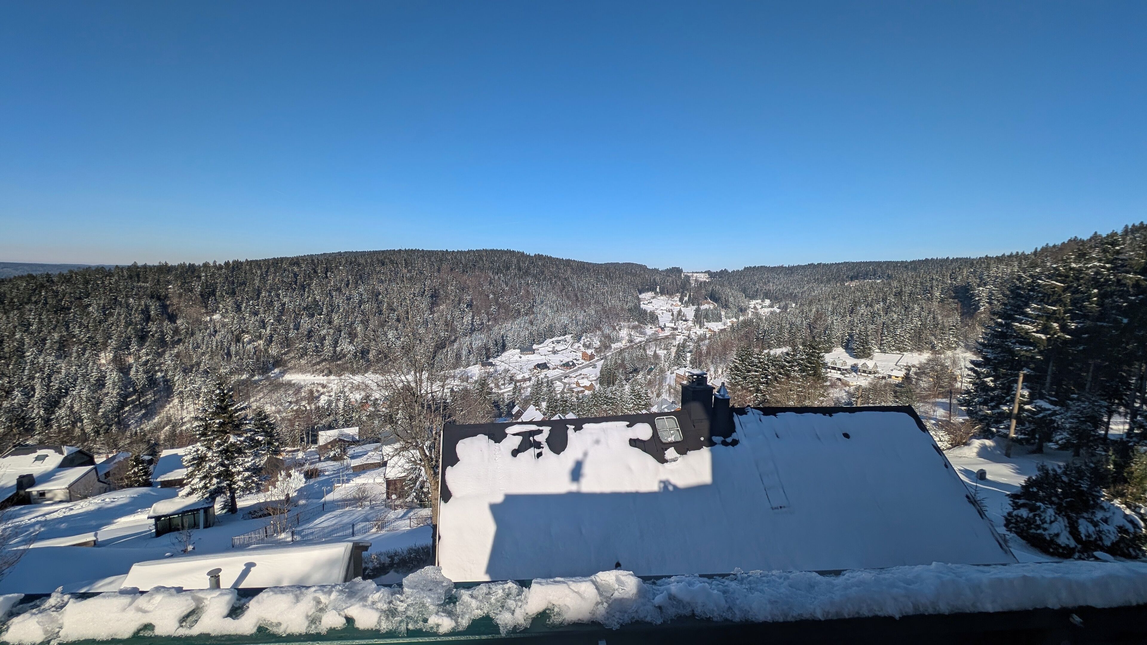 Eine verschneite Landschaft mit einem Gebäude, das ein flaches Dach und einen Schornstein hat.