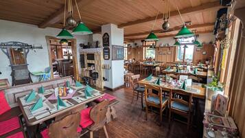 Un restaurante acogedor con interiores de madera, lámparas colgantes verdes y mesas y sillas ordenadas.