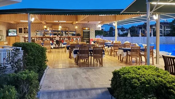 An outdoor dining area with multiple tables and chairs, a covered seating area, and a pool in the background. - Side Ozgurhan Hotel (Manavgat)