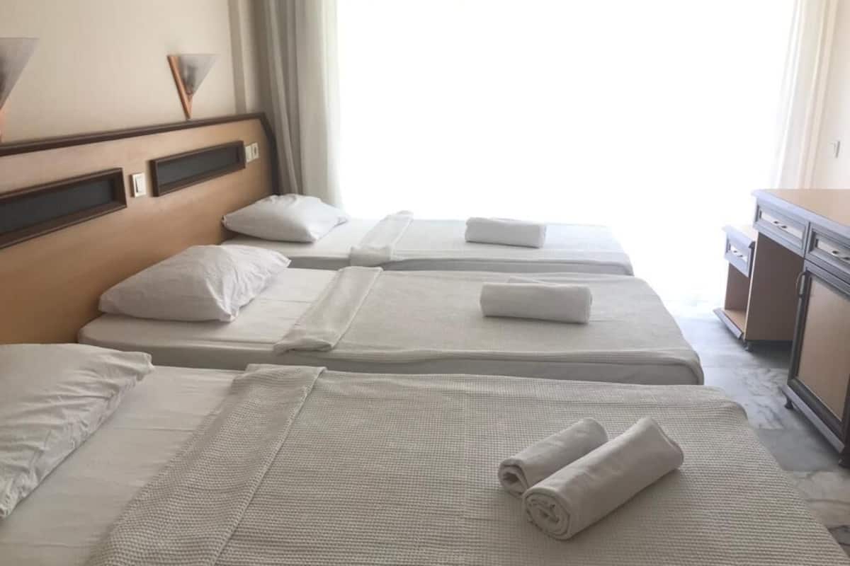 Une chambre d’hôtel avec trois lits, chacun doté de draps et d’oreillers blancs, et d’une tête de lit en bois.
