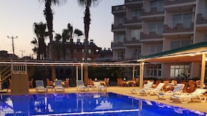 A swimming pool with lounge chairs and umbrellas, surrounded by palm trees and buildings. - Side Ozgurhan Hotel (Manavgat)