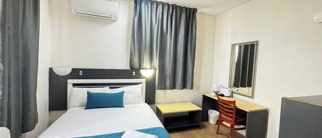 A hotel room with a bed, a desk, a chair, a mirror, an air conditioning unit, and a ceiling fan.