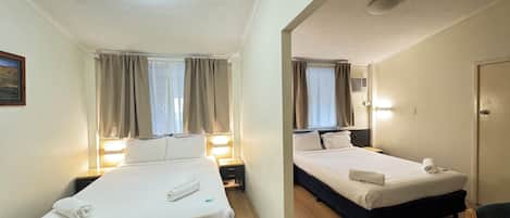 Une chambre d’hôtel avec deux lits simples, un bureau, une chaise, un miroir et un luminaire au plafond.