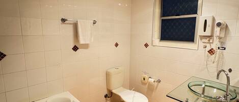 A bathroom with a white bathtub, a glass sink, a toilet, and a window.