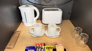 A breakfast setup with a coffee maker, toaster, two cups, a box of biscuits, and various coffee pods. - Taree Motor Inn (Taree)