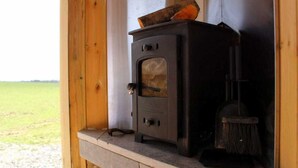 A wood-burning stove in a wooden cabin with a view of a grassy field. - The Shearer's Hut, Sleeps 2, Wood Burner, Fire Pit (Carmarthen)