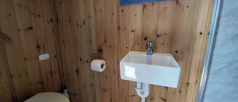 Ett litet badrum med träpanel på väggarna, ett vitt handfat, en toalett och ett fönster ovanför handfatet.