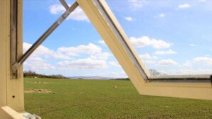 A view through a window with a metal frame, looking out at a green field and a clear sky with clouds. - The Shearer's Hut, Sleeps 2, Wood Burner, Fire Pit (Carmarthen)