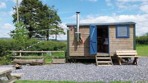 A small wooden cabin with a blue door, a chimney, and a window. - The Shearer's Hut, Sleeps 2, Wood Burner, Fire Pit (Carmarthen)