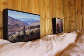 A bedroom with two paintings on the wall, a bed with white bedding, and wooden paneling.