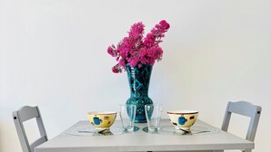 Una mesa de comedor con dos sillas, un florero con flores rosas y dos cuencos con diseño de taza de café.