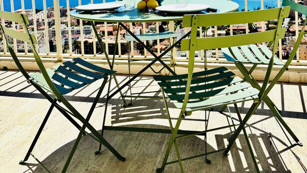 Un balcón con mesa, sillas, un florero con flores y vista al mar.