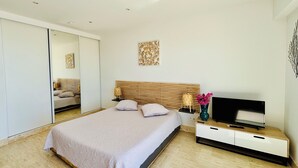 Un dormitorio moderno con una cama grande, un televisor sobre una consola de madera, un espejo y una obra de arte en la pared.