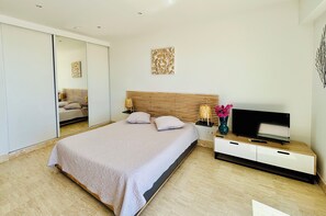 Un dormitorio moderno con una cama grande, un televisor sobre una consola de madera, un espejo y una obra de arte en la pared.