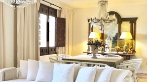 A living room with a white sofa, a dining table with chairs, a chandelier, and a painting on the wall.