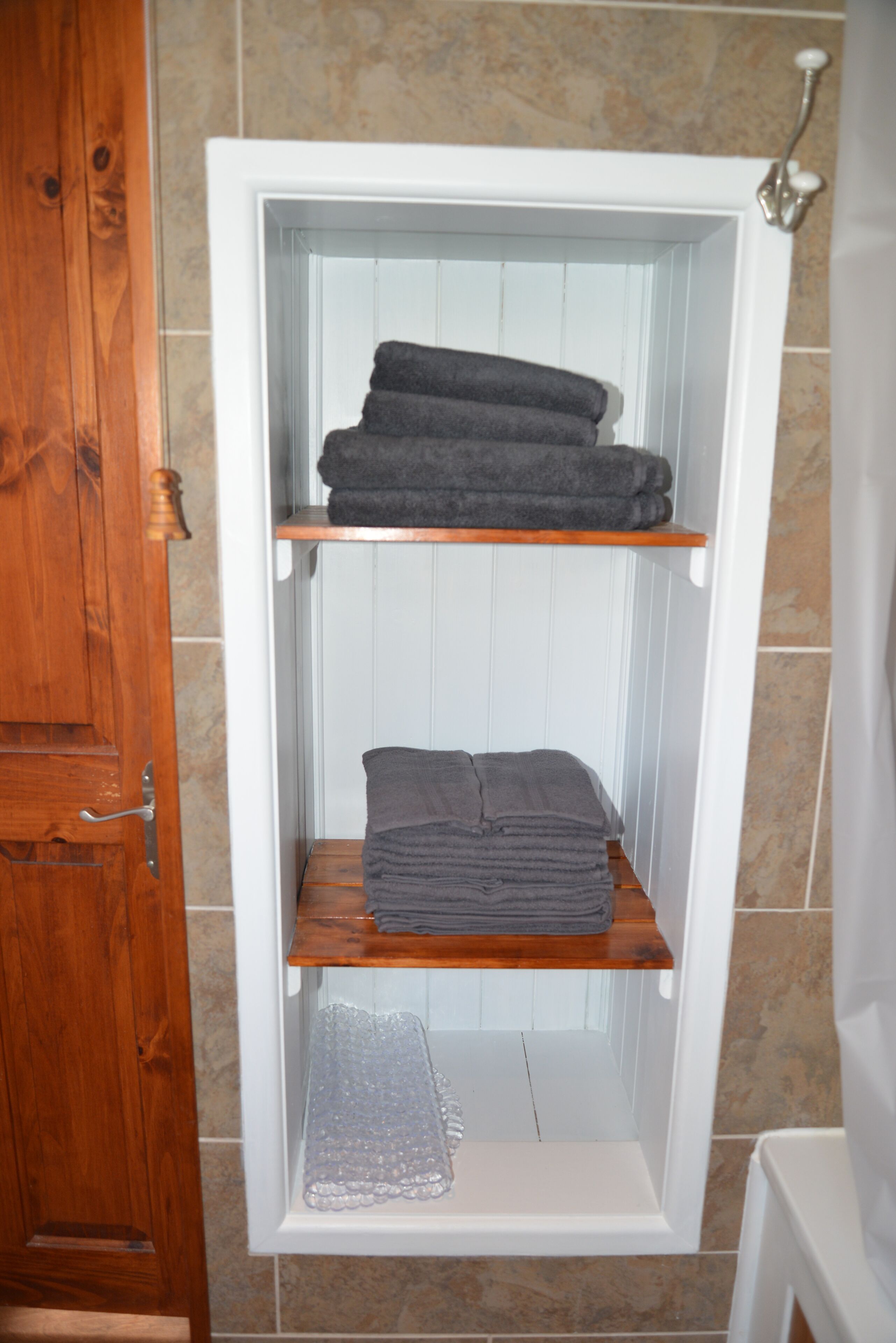 A bathroom with a wooden door, a white bathtub, and a towel rack with folded towels.