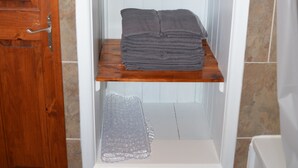 A bathroom with a wooden door, a white bathtub, and a towel rack with folded towels. - Atlantic Retreat - 5 minute stroll from Crooklets Beach (Bude)