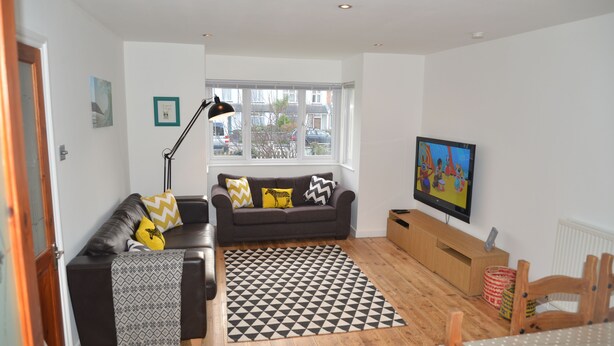 A living room with a sofa, a patterned rug, a television, and a window with a view of the outside. - Atlantic Retreat - 5 minute stroll from Crooklets Beach (Bude)