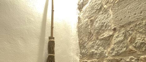 A broom leaning against a wall with a textured stone surface.
