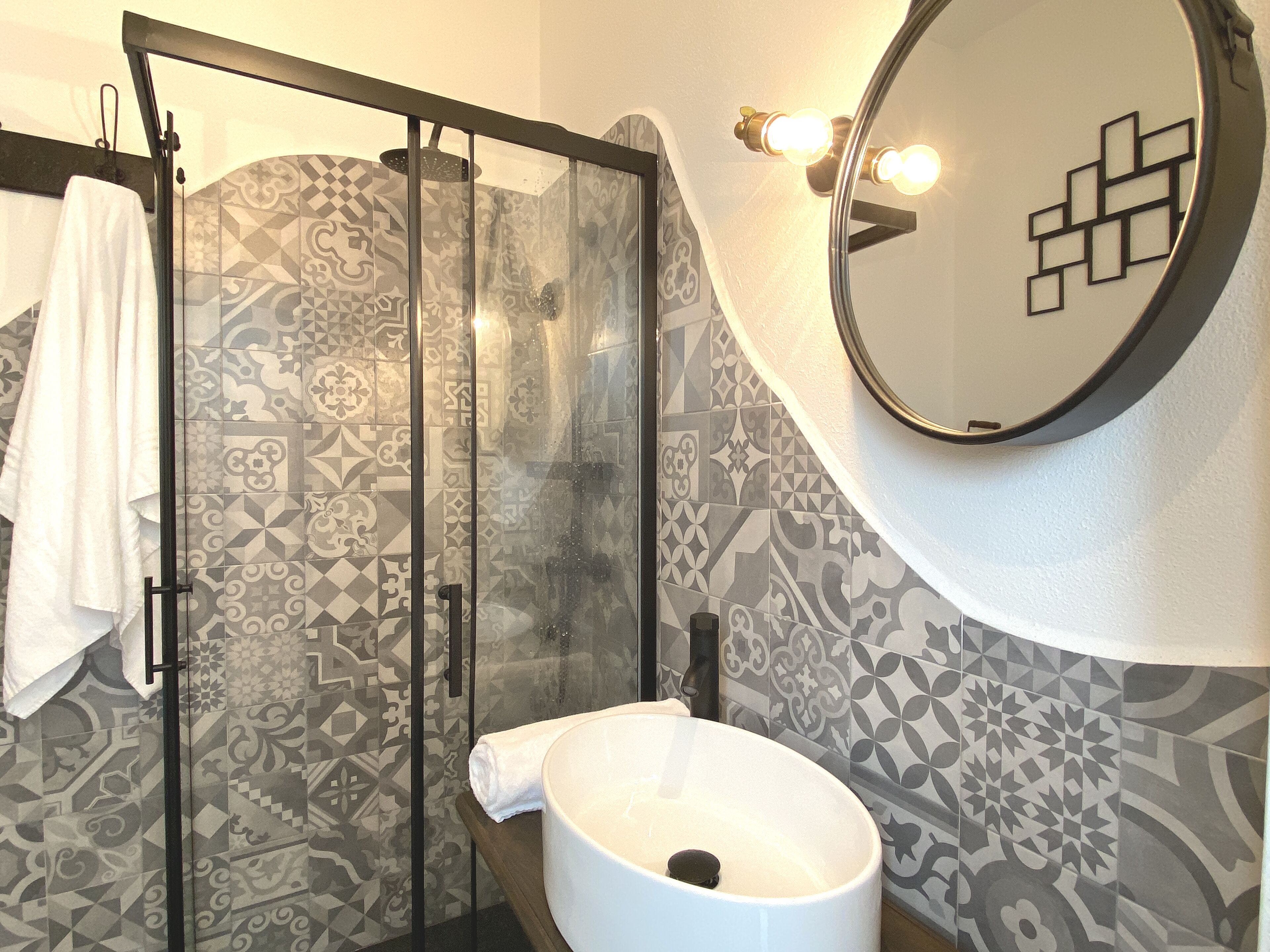 A bathroom with a glass-enclosed shower, a white sink, and patterned tiles.