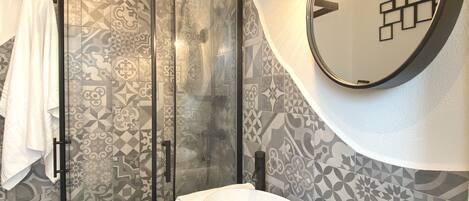 A bathroom with a glass-enclosed shower, a white sink, and patterned tiles.