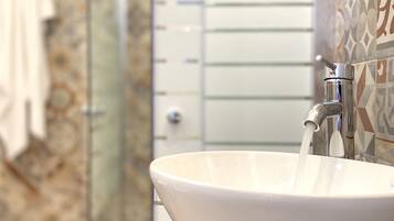 A bathroom with a white sink, a glass shower enclosure, and patterned tiles on the walls.