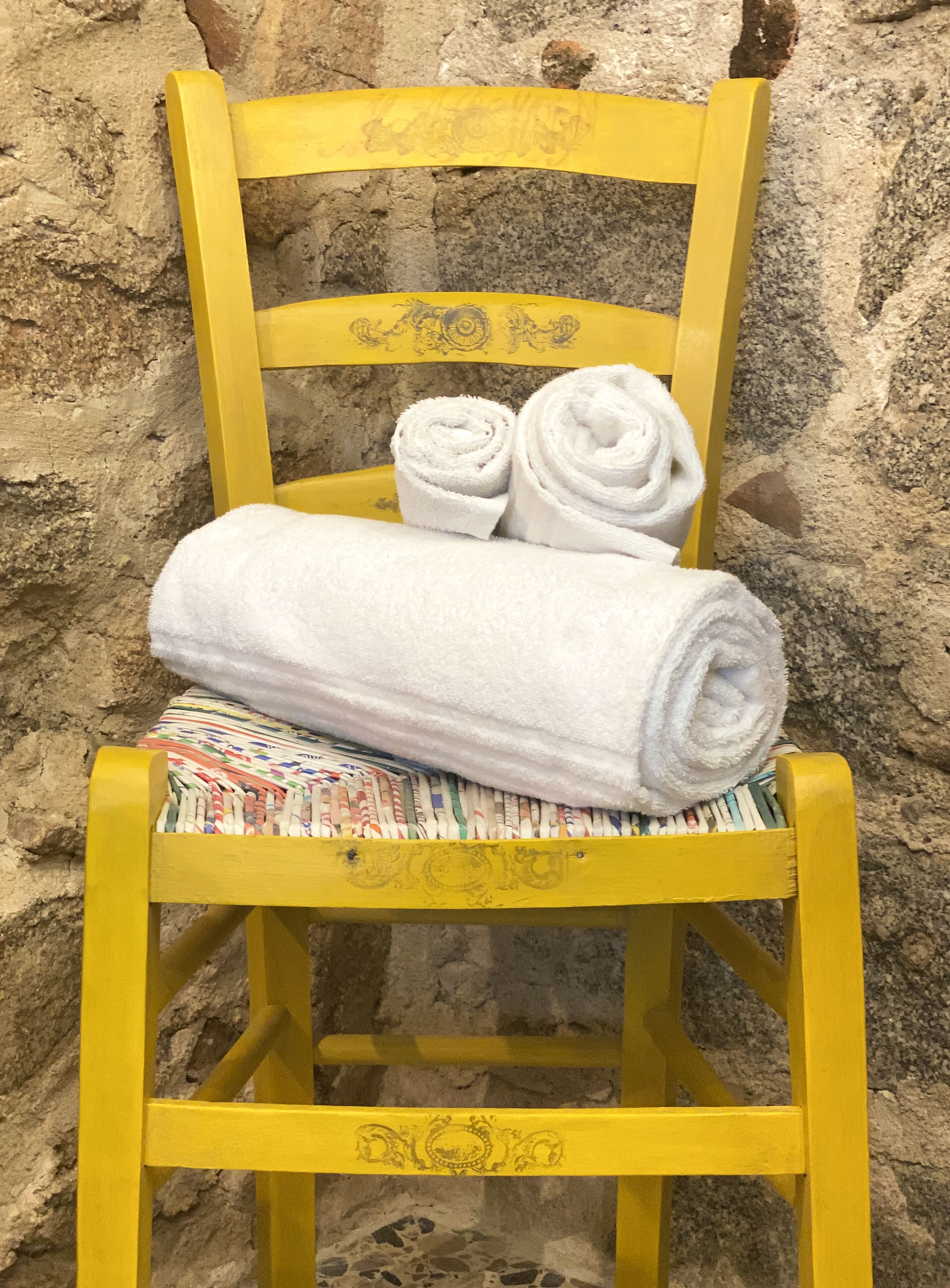 Una silla amarilla con toallas blancas enrolladas y una toalla colorida.