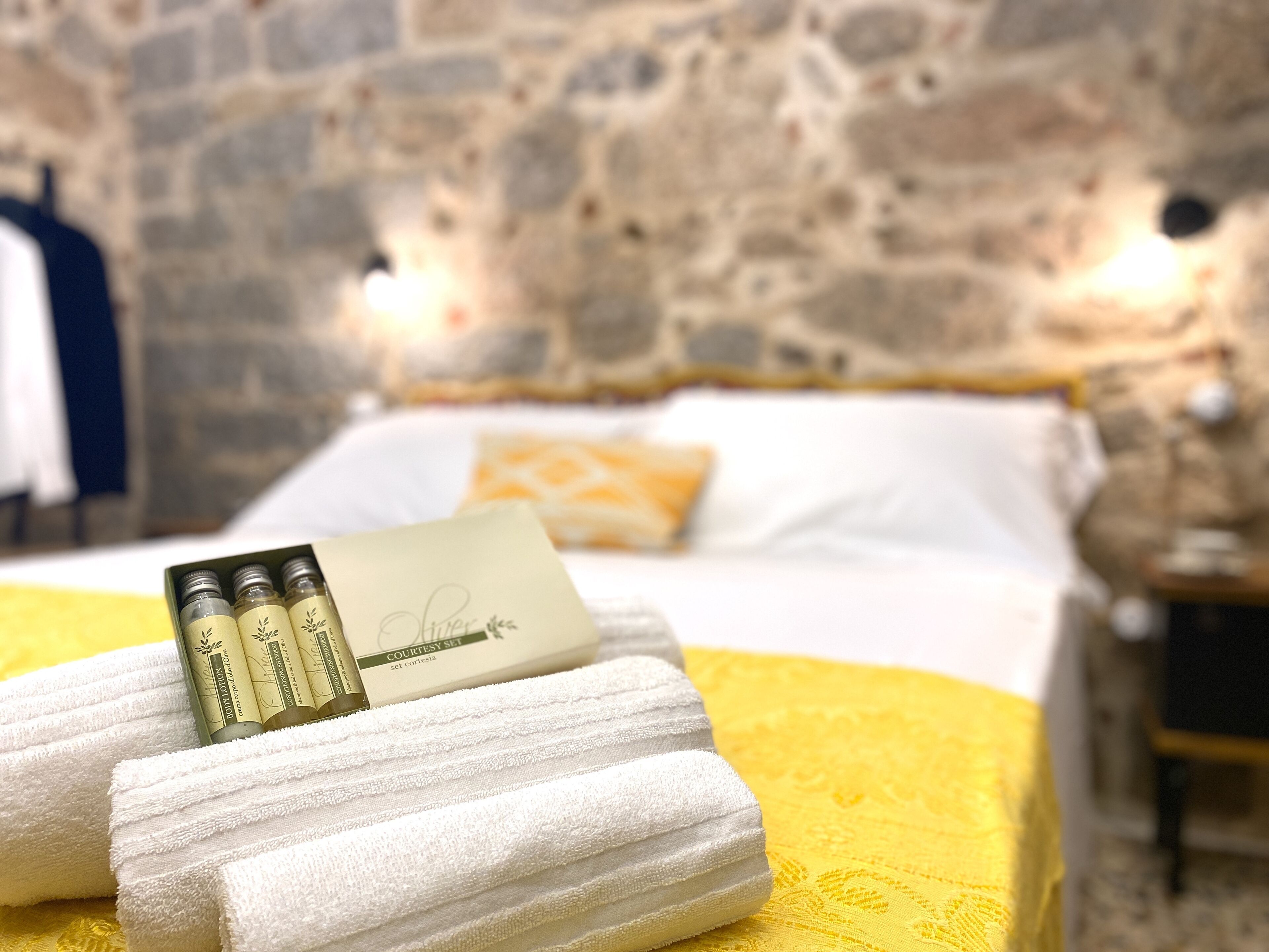 A neatly made bed with a yellow bedspread, a white pillow, and a set of toiletries on a white towel.
