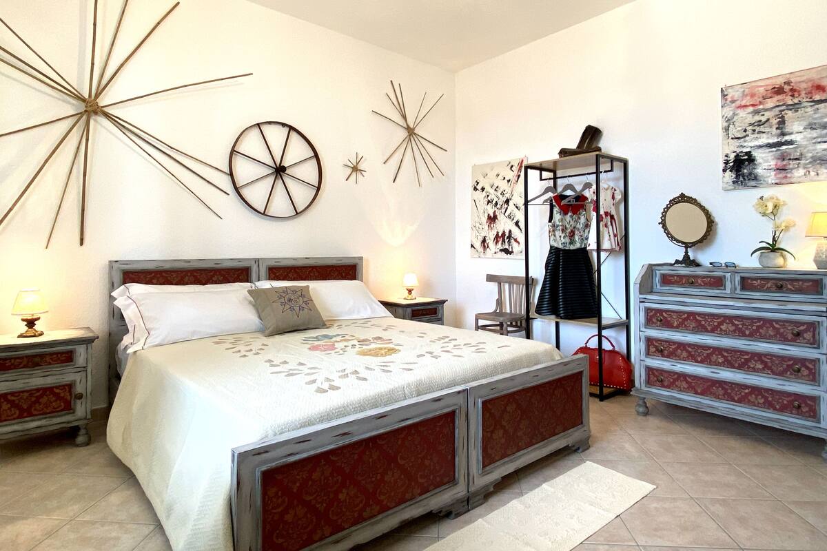A bedroom with a large bed, a dresser, a chair, and wall decorations.