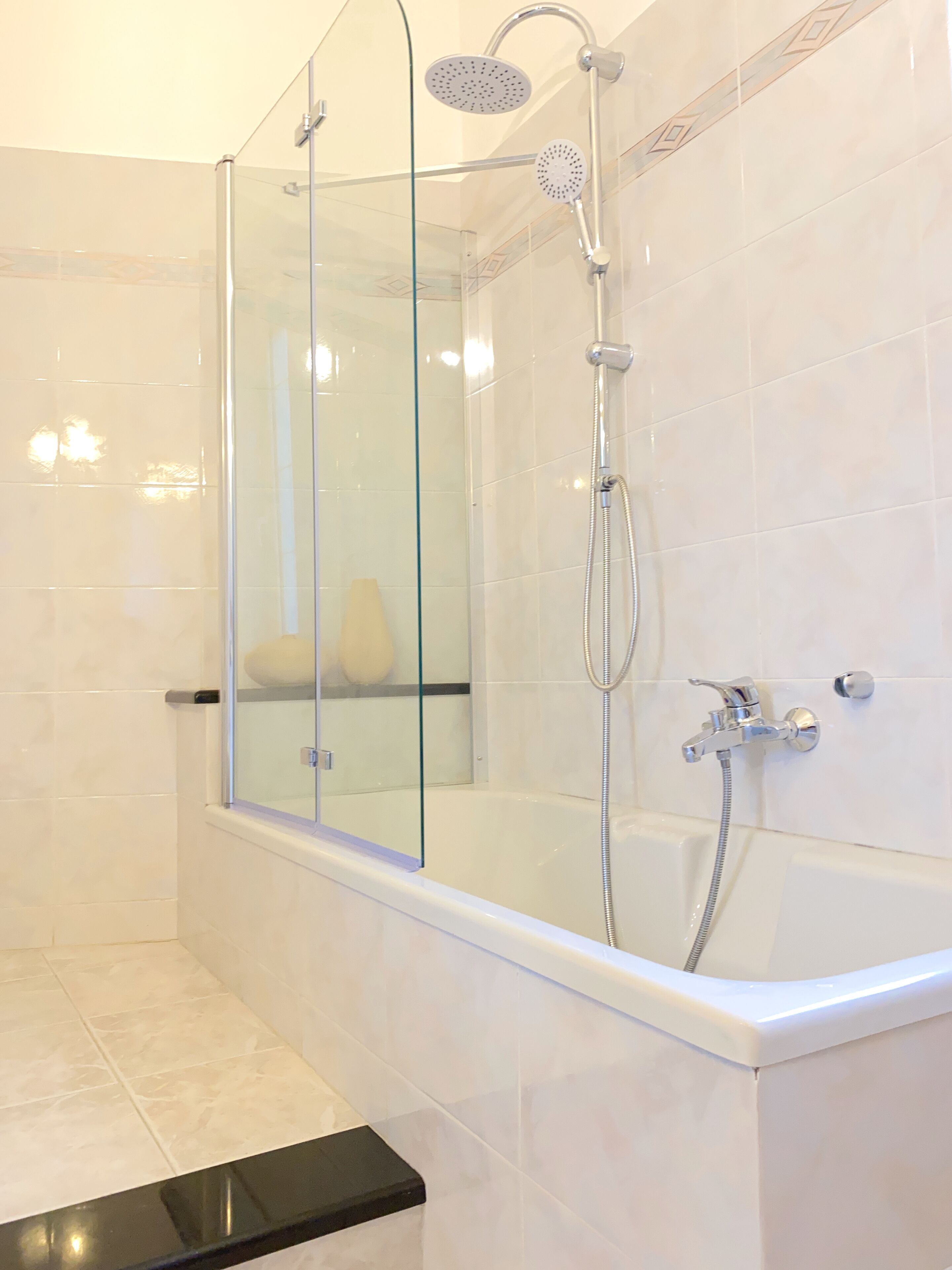A modern bathroom with a glass-enclosed shower, a white bathtub, and a black countertop.