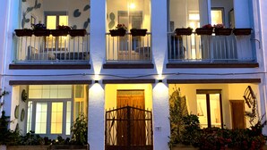A multi-story building with balconies, large windows, and outdoor lighting. - Canduleri (Orgosolo)