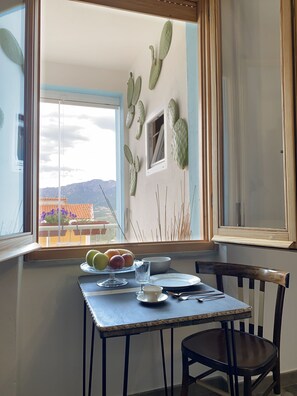 A dining area with a table set for two, a window with a view of mountains, and cacti on the wall.