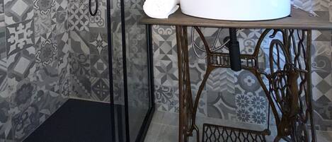 A bathroom with patterned tiles, a glass shower enclosure, a sink with a mirror, and a vintage sewing machine table.