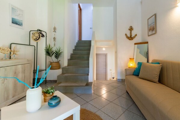 A living room with a sofa, a coffee table, a staircase, and a dining area with a table and chairs. - Villa marta, just 100 m from Cala Caterina (villasimius)