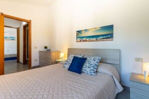 A bedroom with a bed, a nightstand, a lamp, a painting, and a door leading to another room. - Villa marta, just 100 m from Cala Caterina (villasimius)